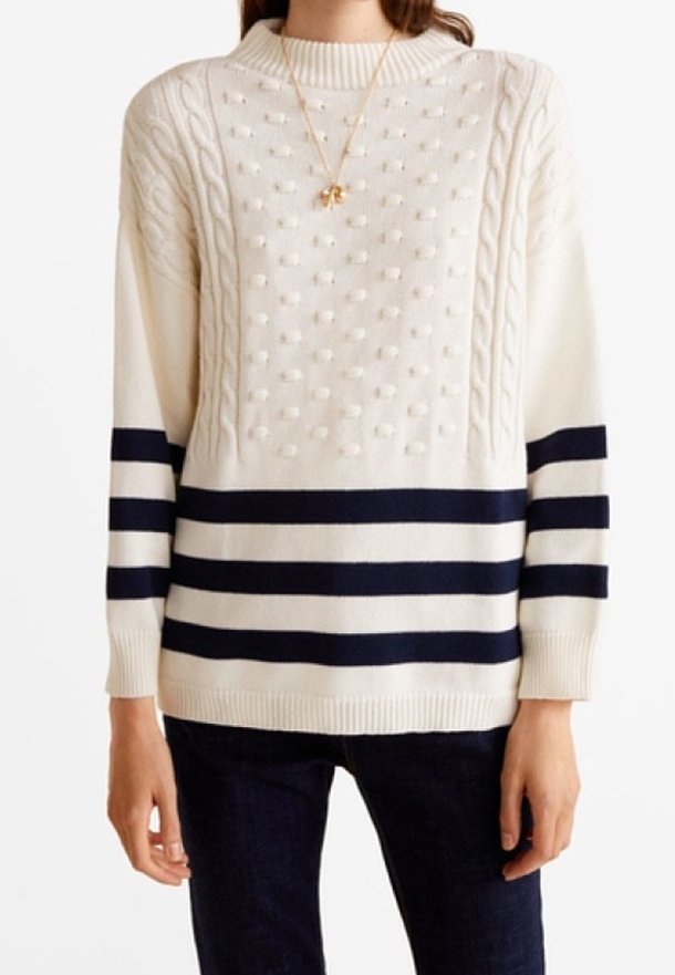 Femme portant un pull en tricot crème avec un motif texturé à boules et des rayures horizontales bleu marine aux manches et en bas du vêtement, associé à un pantalon foncé.