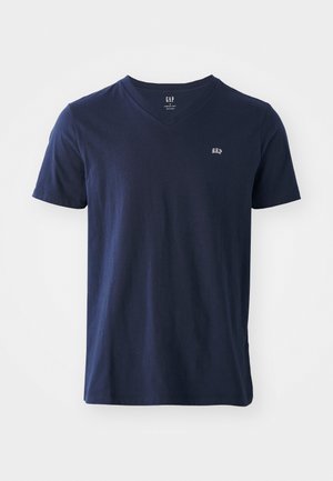 Tumedast sinine puuvillane T-särk V-kaelusega, lühikeste varrukatega ja väikese tikitud logoga rinnal. Pehme tekstuur ja lõdva disain.