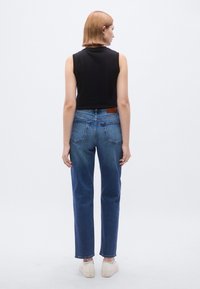 Εφαρμοστή μαύρη αμάνικη μπλούζα. Μπλε τζιν με ίσια μπατζάκια, μέση μεσαίας στάθμης, δύο πίσω τσέπες και καφέ δερμάτινο ταμπελάκι στη ζώνη.