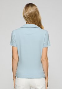 Light blue polo shirt with a collar and short sleeves. Smooth texture, fitted design. Minimalist style with no visible patterns or accents.