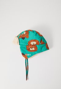Casquette d'enfant en tissu turquoise avec des motifs d'ours brun, doublée de fourrure blanche et équipée de liens pour un ajustement sécurisé. Le texte indique "TINY."