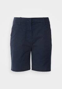 Marinblå knä-långa shorts med bältesöglor, framfickor och en dold framknäppning mot en enfärgad ljus bakgrund.