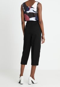 Svarta cropped byxor som matchas med en flerfärgad mönstrad topp med rundad halsringning och dekorativa band, vilket kompletteras av vita blockklackskor.