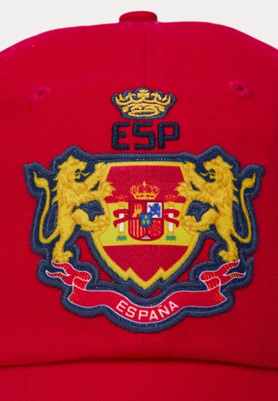 Červená čepice s vyšitým žlutým a modrým erbem s lvy, korunou a slovy "ESPAÑA" na texturované tkanině.