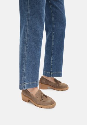 Mocassini in camoscio marrone con dettaglio tassel e suola in gomma, abbinati a jeans dritti blu, che mostrano uno stile di calzature casual.