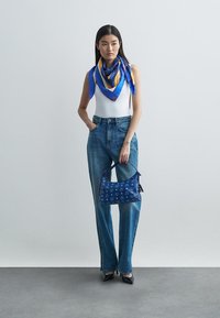 Lysblå denimbukser med høj talje og sidesyninger, hvid ærmeløs top og en blå mønstret handbag. Blå og guld silkeslør.