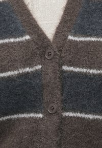 Hnedo-šedý pletený sveter s chlpatou textúrou, so zvislými pruhmi, výstrihom do V a dvomi tmavými gombíkmi vpredu.