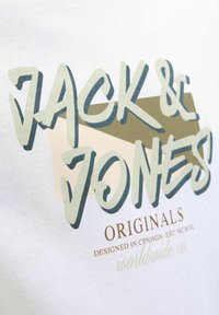 Hvid bomulds t-shirt med fed, lagdelt tekst i grøn og beige, med "JACK & JONES" øverst og "ORIGINALS" nedenunder i brun.
