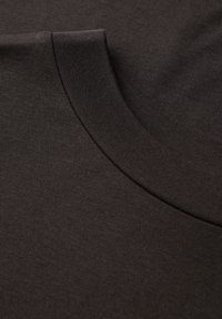 Tessuto di cotone marrone scuro con una texture liscia, caratterizzato da un collo rotondo e da un motivo a maglia sottile e uniforme. Modellato per il comfort.
