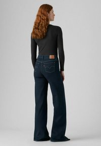Un jean bleu foncé taille haute avec une coupe décontractée et des jambes larges, arborant un classique patch en cuir Levi's sur la ceinture arrière.