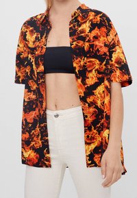 Kortärmad skjorta med ett djärvt flammönster i orange och gult på svart bakgrund. Knappförsedd design med bröstficka.