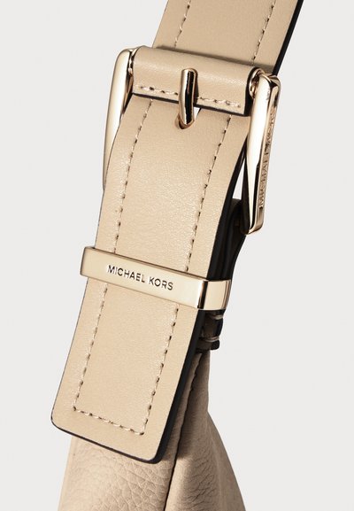 Бежова кожена каишка със златиста катарама и обръч, щампована с логото на "MICHAEL KORS", прикрепена към текстуриран кожен материал на чанта.