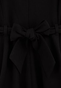 Crna haljina s detaljem mašne oko struka, izrađena od meke, mat tkanine s glatkom teksturom i preciznim, čistim šavovima.