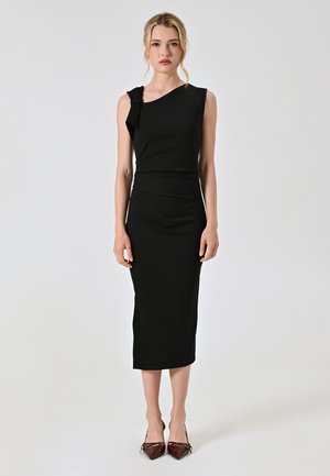 Schwarzes Midi-Kleid mit asymmetrischem Ausschnitt und Rüschendetails. Glatter, enganliegender Stoff mit schlanker Silhouette, kombiniert mit spitzen bordeauxfarbenen Absätzen.