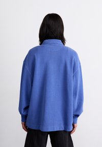 Oversized blue sweatshirt, cotton fabric, ribbed cuffs, and collar, dropped shoulders, stitched accents, and a straight hem.