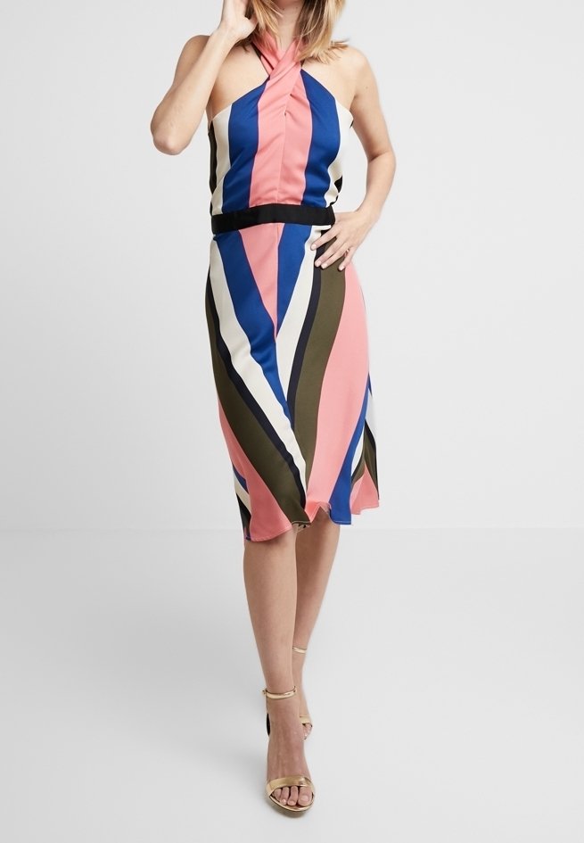 Femme portant une robe sans manches à col licou avec des rayures verticales rose, bleu, blanc et olive, associée à des sandales dorées à bride autour de la cheville.