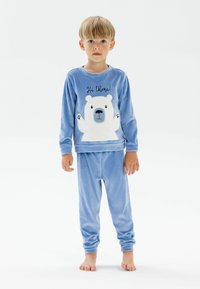 Pijamale din fleece de culoare albastră deschisă, cu un grafic al unui urs polar alb și textul "Salut!". Mâneci lungi și manșete elastice, textură moale, croială lejeră.