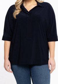 Marineblå oversized blouse med krave, korte ærmer og en glat tekstur, parret med tætsiddende denim jeans.