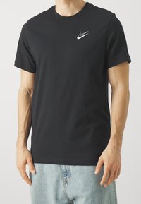 Black cotton t-shirt with short sleeves, featuring a white Nike logo on the left chest, smooth texture, and standard crew neckline.