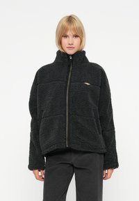 Schwarze Fleecejacke mit hohem Kragen, Reißverschlussfront und Seitentaschen. Sie verfügt über ein strukturiertes Muster und elastische Bündchen.