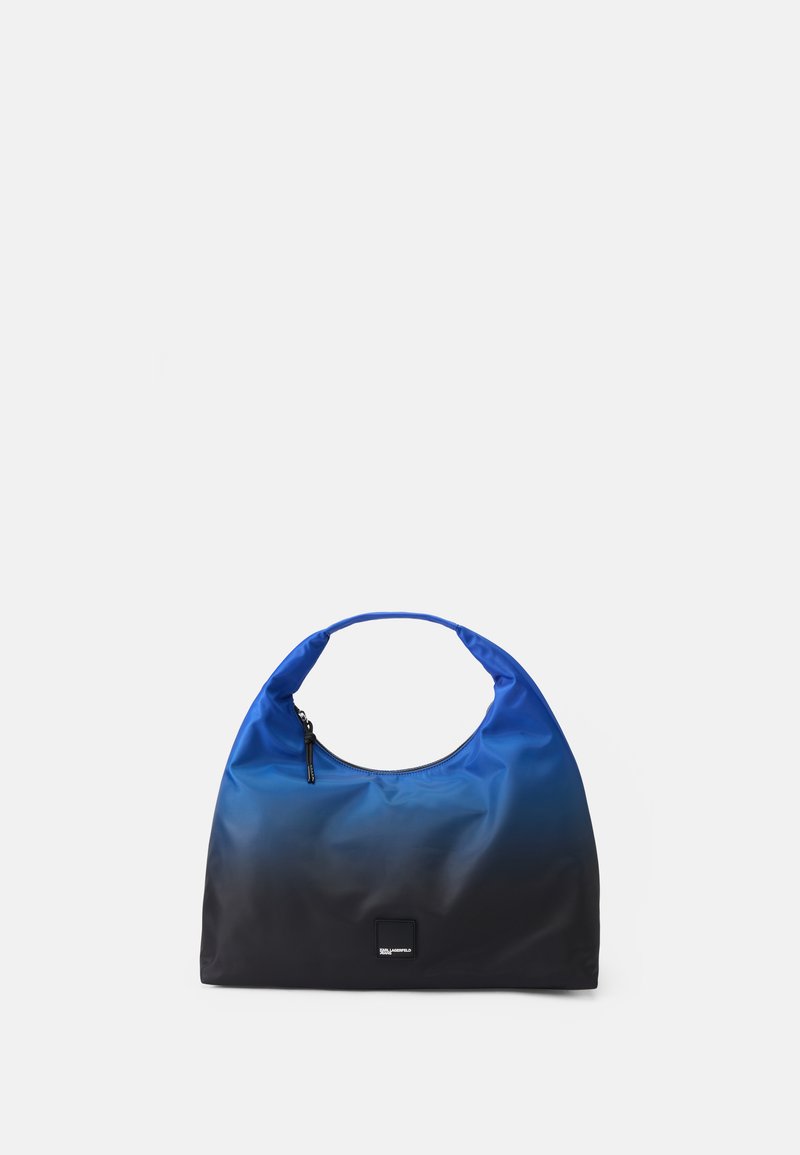 Mėlyna ir juoda gradientinė rankinė pagaminta iš nailono, turinti kreivos formos rankeną, užtrauktuko užsegimą ir kvadratinį logotipo pleistrą priekyje.