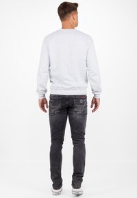 Felpa grigia con scollatura rotonda, abbinata a jeans neri slim-fit con tasche posteriori e sneakers bianche. Design semplice e casual.