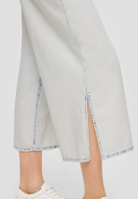 Białe dżinsowe kuloty z niebieskim kontrastowym przeszyciem, z bocznymi rozporkami na dole i prostym krojem, zestawione z białymi sneakersami.