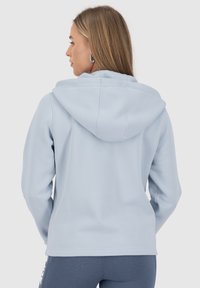Felpa con cappuccio azzurro chiaro con una finitura testurizzata, caratterizzata da un cappuccio con cordino e una vestibilità comoda, abbinata a leggings sportivi blu scuro.