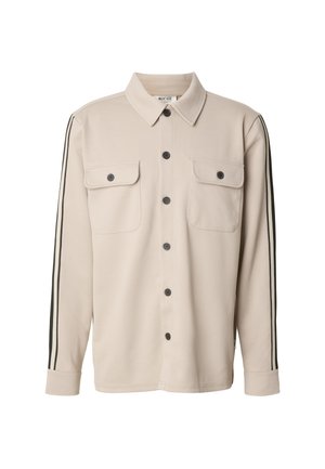 Camicia beige a maniche lunghe con chiusura frontale con bottoni, due tasche sul petto e strisce nere sui lati. Realizzata in un tessuto liscio e strutturato.