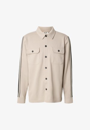 Camicia beige a maniche lunghe con chiusura frontale con bottoni, due tasche sul petto e strisce nere sui lati. Realizzata in un tessuto liscio e strutturato.