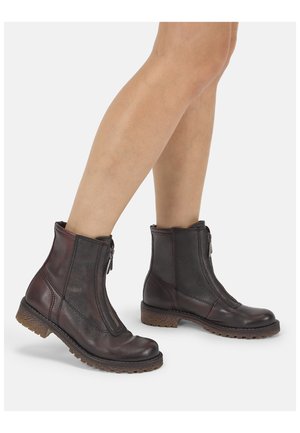 Pair of dark brown leather ankle boots with front zippers worn on bare legs, showing textured soles and rounded toes.