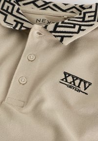 Béžová polokošeľa s čiernobielym vzorovaným golierom, tromi gombíkmi a čiernym vyšitým nápisom "XXIV SEVEN" na prednej strane. Materiál: bavlna.