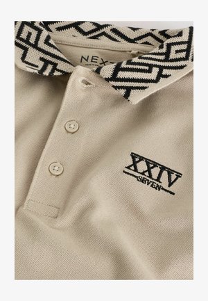 Béžová polokošeľa s čiernobielym vzorovaným golierom, tromi gombíkmi a čiernym vyšitým nápisom "XXIV SEVEN" na prednej strane. Materiál: bavlna.