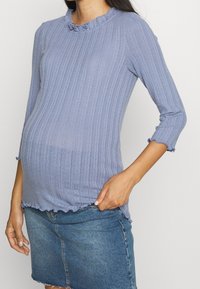 Ljust blå ribbad graviditetstopp med volangkrage och trekvartsärmar, med en åtsittande design och en texturerad tyg.