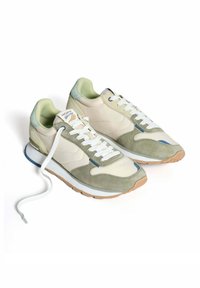 Zapatillas en gamuza beige claro y verde, con cordones blancos, lengua acolchada y suela de goma. Presenta un acento azul en el lateral.