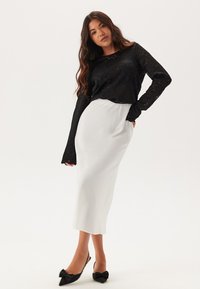 Schwarzes Spitzenoberteil mit langen Ärmeln, kombiniert mit einem weißen, taillierten Midikleid. Verfügt über eine glatte Textur und schwarze High Heels mit Schleifenakzent.
