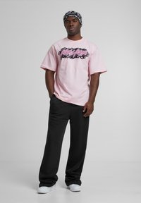 Light pink short-sleeve t-shirt with a black and pink graphic print, paired with black wide-leg pants and white sneakers. Black-and-white patterned beanie.