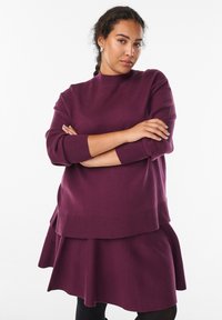 Violetti kerrosneule ja hame -setti, jossa on korkea kaulus, pitkät hihat ja leveneviä helmoja. Pehmeä rakenne ja ribbireunukset.