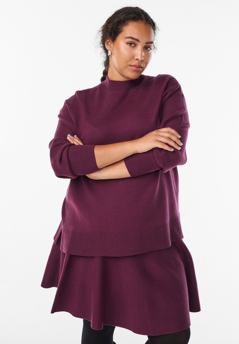 Violetti kerrosneule ja hame -setti, jossa on korkea kaulus, pitkät hihat ja leveneviä helmoja. Pehmeä rakenne ja ribbireunukset.