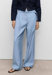 Helle blaue, locker sitzende Hose aus glattem Stoff mit Vorderfalten und hoher Taille, kombiniert mit einer dunklen, taillierten Jeansjacke.