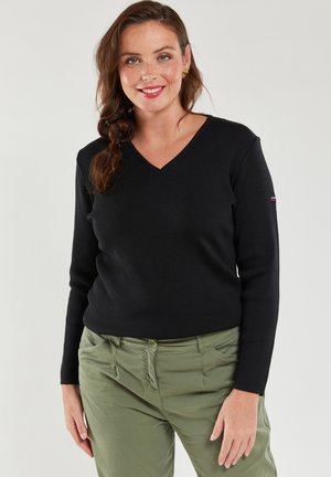 Maglione nero a V in morbido tessuto a coste; design aderente con maniche lunghe; abbinato a pantaloni verdi con tasche frontali.