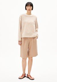 Gestreiftes Langarmhemd in sanftem Beige und Off-White, kombiniert mit lockeren beigen Shorts und schwarzen Sandalen mit roten Akzenten.