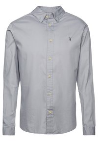 Jasnoszara, długosługa koszula z guzikami i kołnierzykiem, z kremowymi guzikami oraz małym, ciemnym, haftowanym logo zwierzęcia po lewej stronie klatki piersiowej.