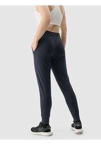 Granatowe spodnie sportowe o slim fit, z elastycznym pasem i bocznymi kieszeniami, wykonane z gładkiego materiału. W zestawie z czarnymi butami do biegania.