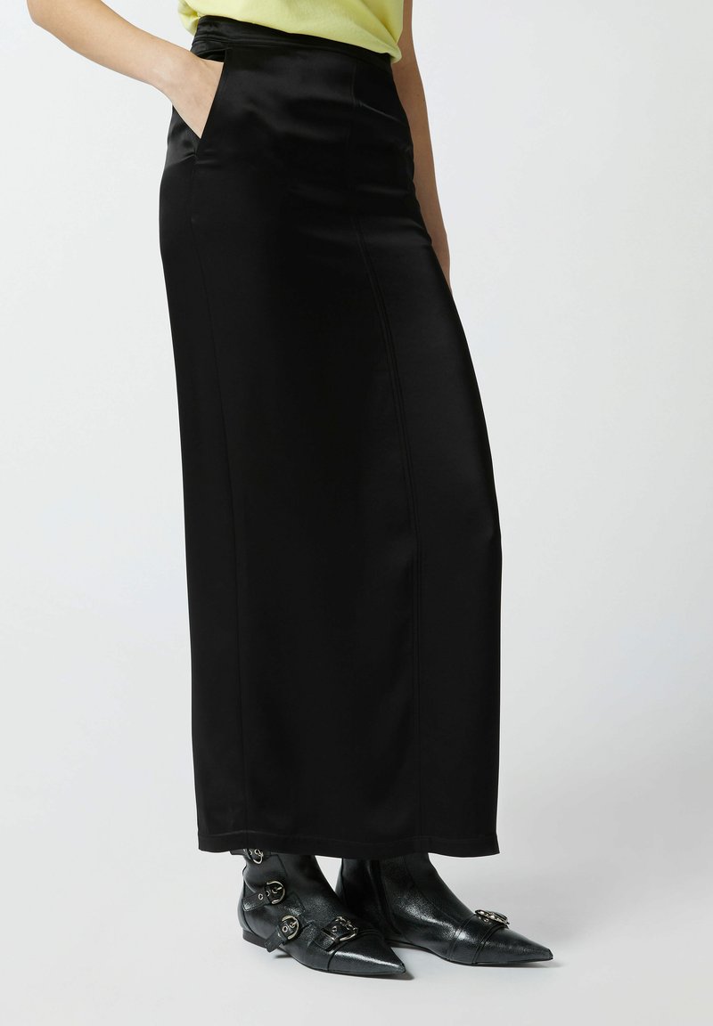 Crna satenska maksi suknja s bočnim džepovima, koja ima glatku teksturu i čiste linije, uparena s crnim čizmama s oštrim vrhom do članaka.