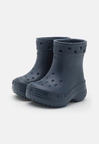 Une paire de bottes en caoutchouc bleu marine avec des semelles texturées et des trous de ventilation, conçues pour offrir protection et confort par temps humide.