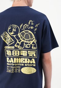Navy cotton t-shirt featuring a large yellow graphic of a turtle, a battery, and Japanese text, with a textured print.