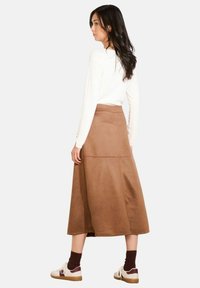 Brown suede midi skirt with a fitted waist, flared shape, and contrasting stitching details. Paired with a white top and sneakers.