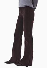 Brązowe spodnie dzwony z wysokim stanem, o teksturowanym wykończeniu i subtelnymi pionowymi liniami, zestawione z ciemnym obuwiem.