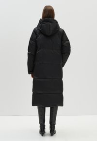 Zwarte pufferjas met een capuchon, met een lange, gewatteerde uitstraling en glanzend, glad materiaal. Strak, vormgevend ontwerp met een moderne uitstraling.